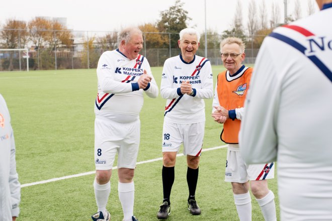 De mannen van Oldstars Walking voetbal staan op het veld met elkaar te lachen